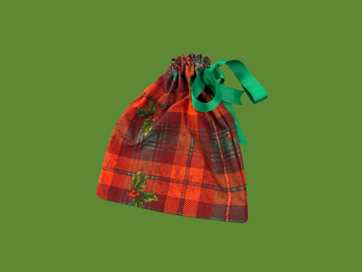 A green background with a red and green plaid cloth drawstring bag with scattered holly on it.